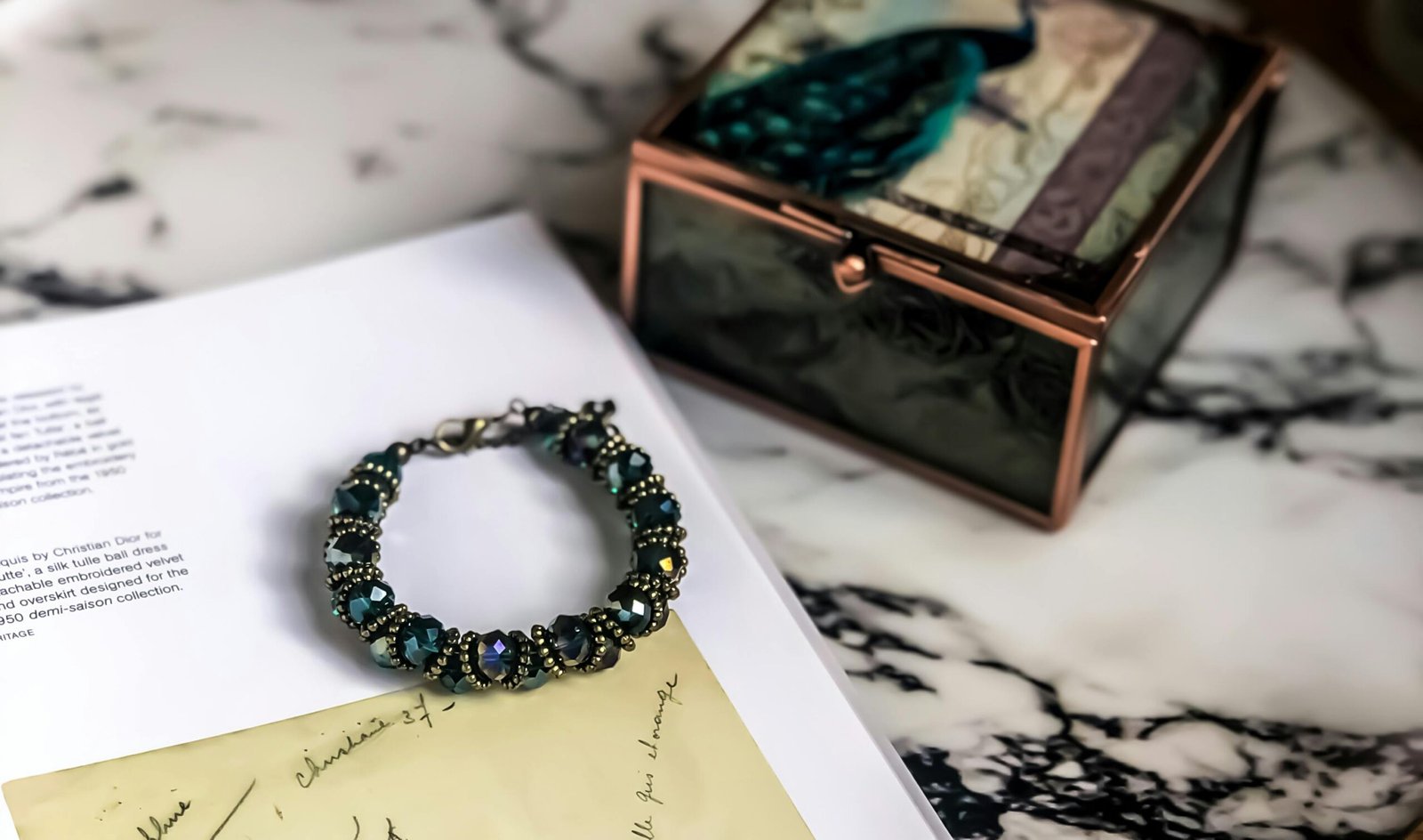 A close-up of a stylish gemstone bracelet resting on a marble surface beside a decorative box.